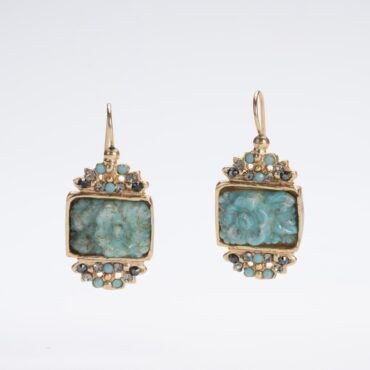 Primo piano di orecchini pendenti "Gioielli d'Autore" su sfondo bianco. I gioielli presentano un medaglione color turchese con una rosa scolpita al centro, incorniciato da cristalli europei color grigio fumo e piccoli turchesi. La finitura in oro 14 KT risplende sulla lega "Demirouge", mettendo in risalto il design artigianale unico.