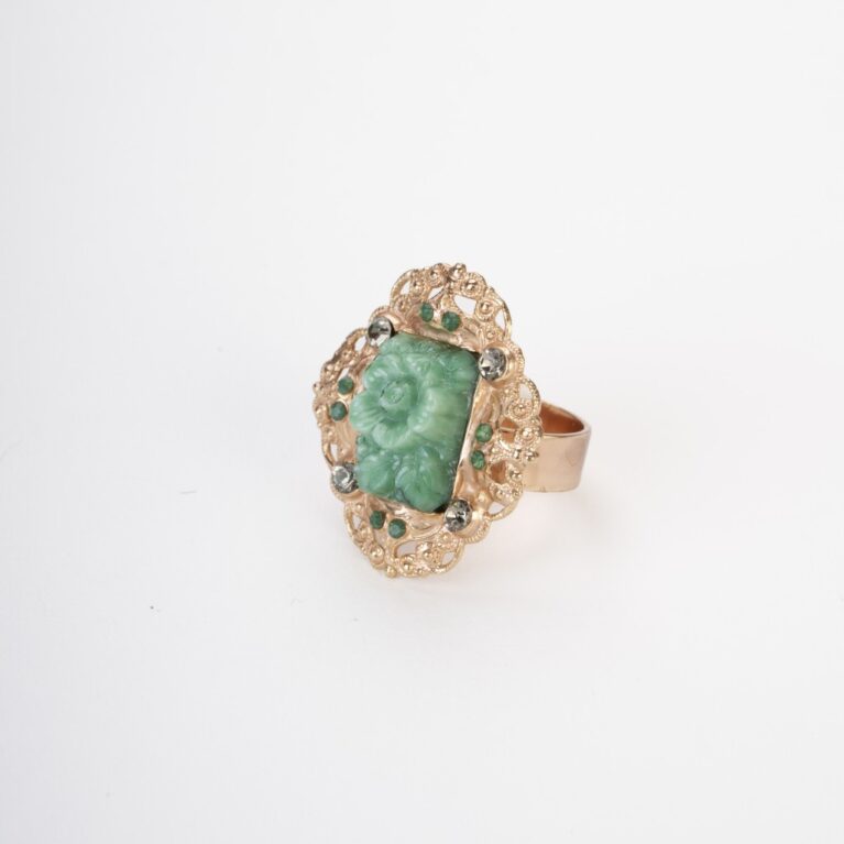Primo piano di un anello artigianale a forma di fiore in pasta vitrea verde giada e cristalli verdi su montatura dorata.