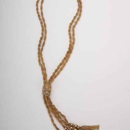 Vista completa della collana sautoir dorata stile cravattino con centrale a testa di leone e quattro frange finali rifinite con nappe dorate su sfondo bianco.
