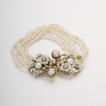 Bracciale Barocco in perle di fiume, stile Vittoriano, con placca in filigrana in ottone e fiori, su sfondo bianco.