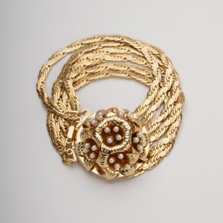 Bracciale multifilo dorato con grande rosone centrale a motivo giglio borbonico e perle su sfondo neutro.