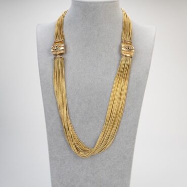 Collana artigianale maestosa in ottone fiammato su busto sartoriale, design materico d'ispirazione templare con cristalli color garnet.