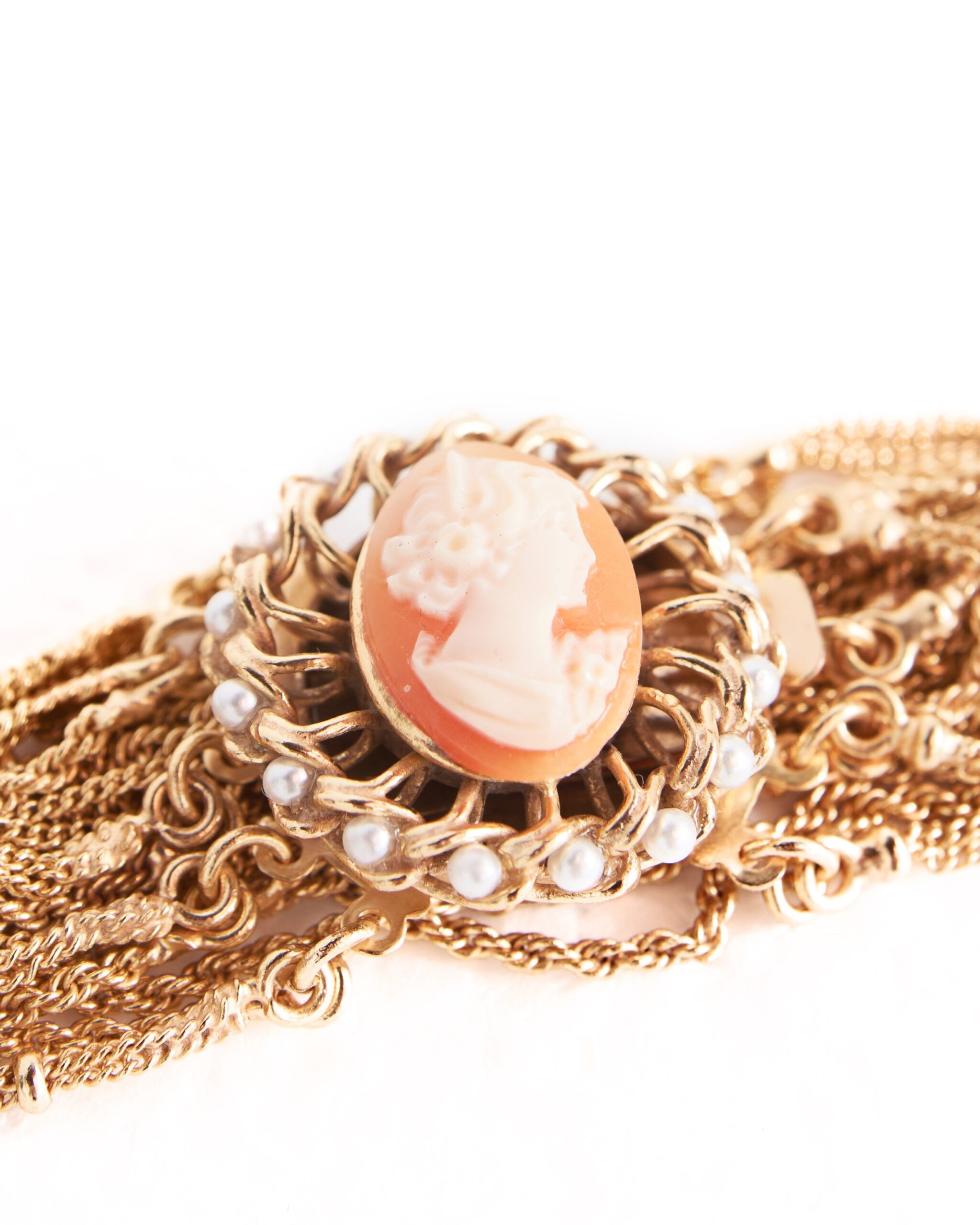Dettaglio di bracciale scultoreo con cammeo e catene dorate multifilo indossato al polso su sfondo chiaro.