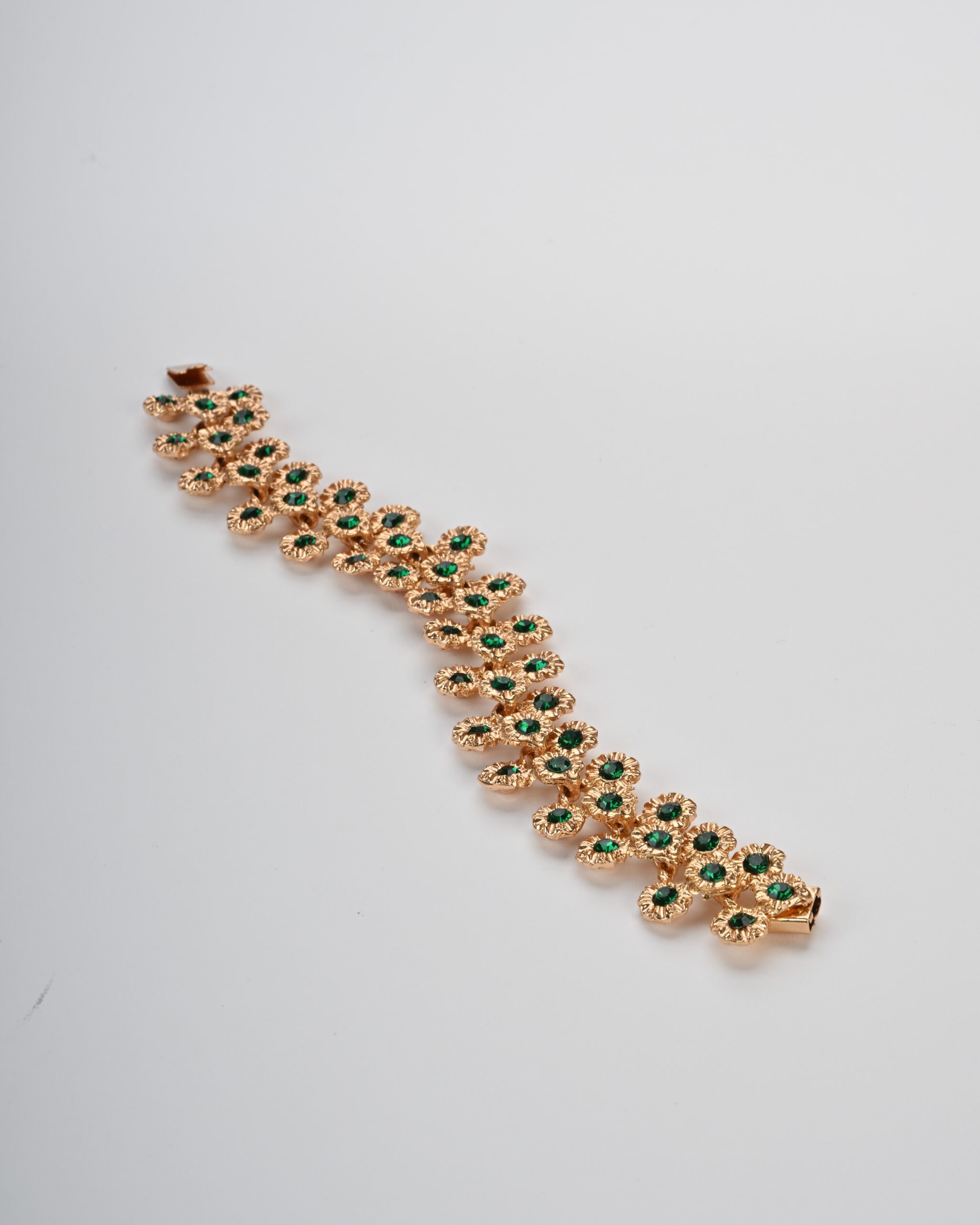 Bracciale a fascia articolata dorata con trama di margherite e cristalli verdi su fondo chiaro