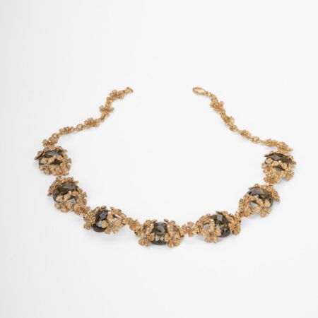 Collana scenografica artigianale Non ti scordar di me in lega demirouge dorata oro 14 KT con fiori scolpiti a mano e cristalli europei color grigio fumo su sfondo bianco