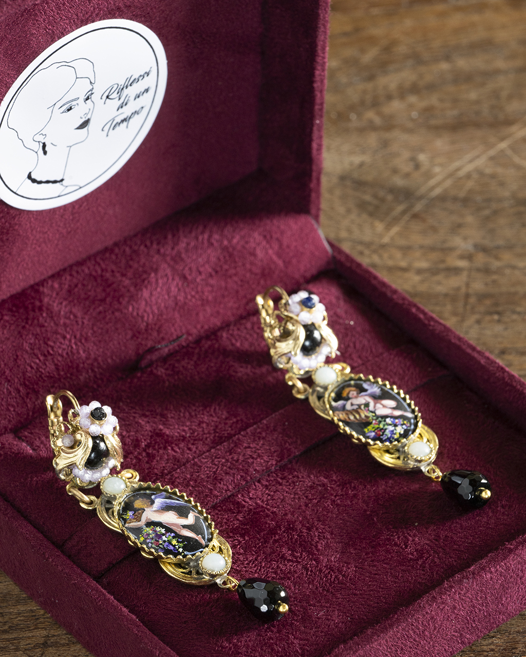 Coppia di orecchini borbonici con miniatura dipinta a mano adagiata all'interno del cofanetto regalo aperto in camoscio bordeaux con logo Riflessi di un Tempo.