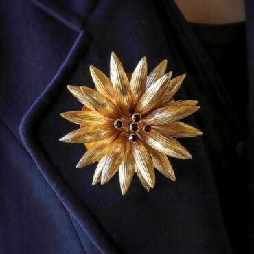Spilla a forma di dalia dorata indossata sul bavero di una giacca scura